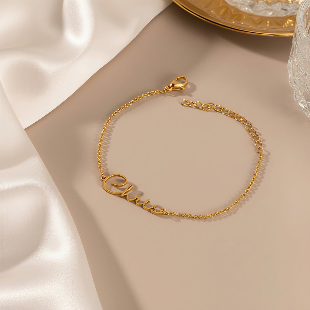 May include: A gold-colored bracelet with the name "Chris" in cursive script. The bracelet is made of a delicate chain and has an adjustable length. The clasp is visible at the end of the chain. The bracelet is displayed on a neutral-toned surface.