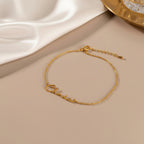 May include: A delicate gold-colored bracelet with the name "Chloe" in cursive script. The bracelet features a fine chain and an adjustable clasp. The jewelry is displayed on a neutral-toned surface, with a soft, white fabric in the background.